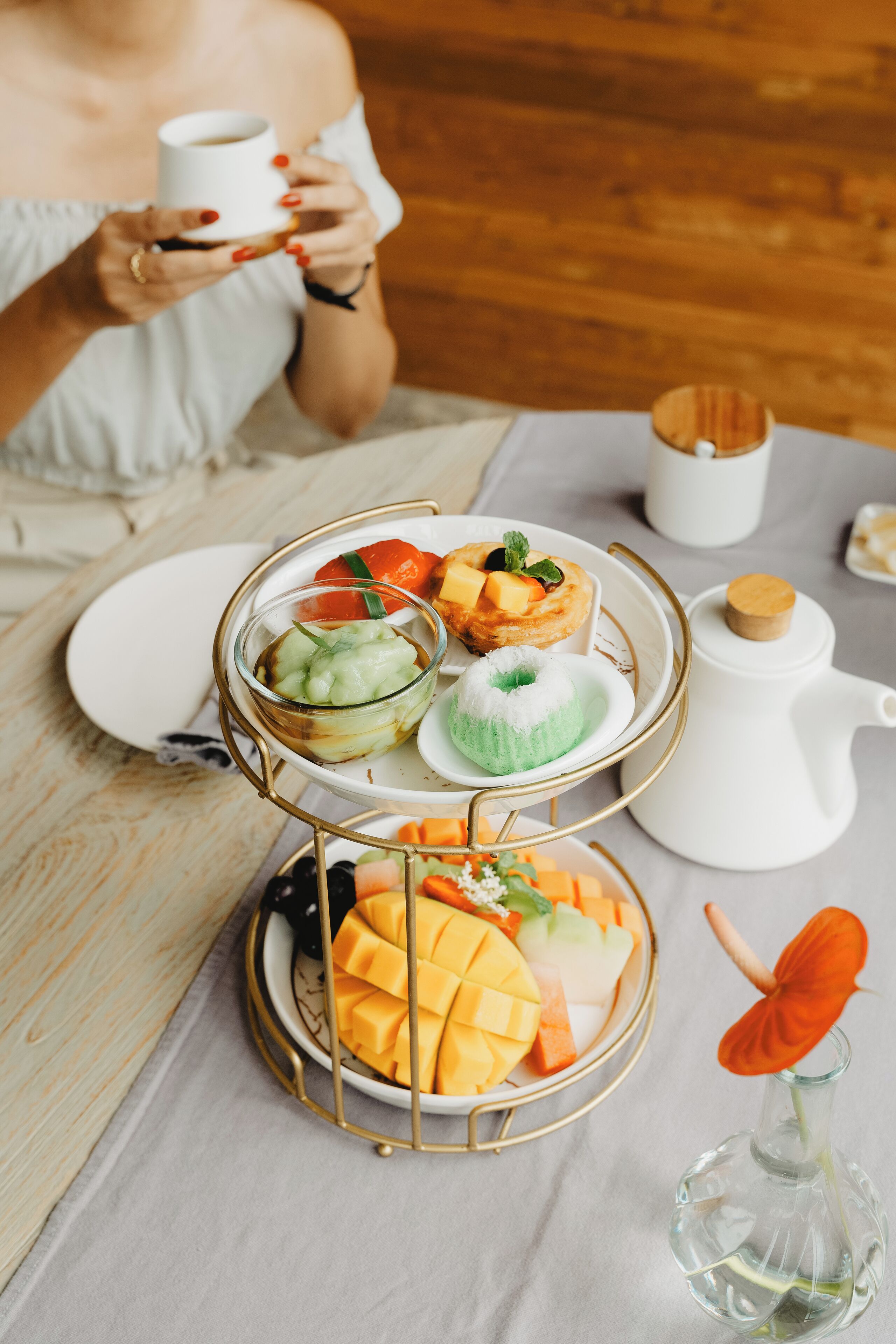 A table with a tiered serving tray holding various desserts and a teapot.