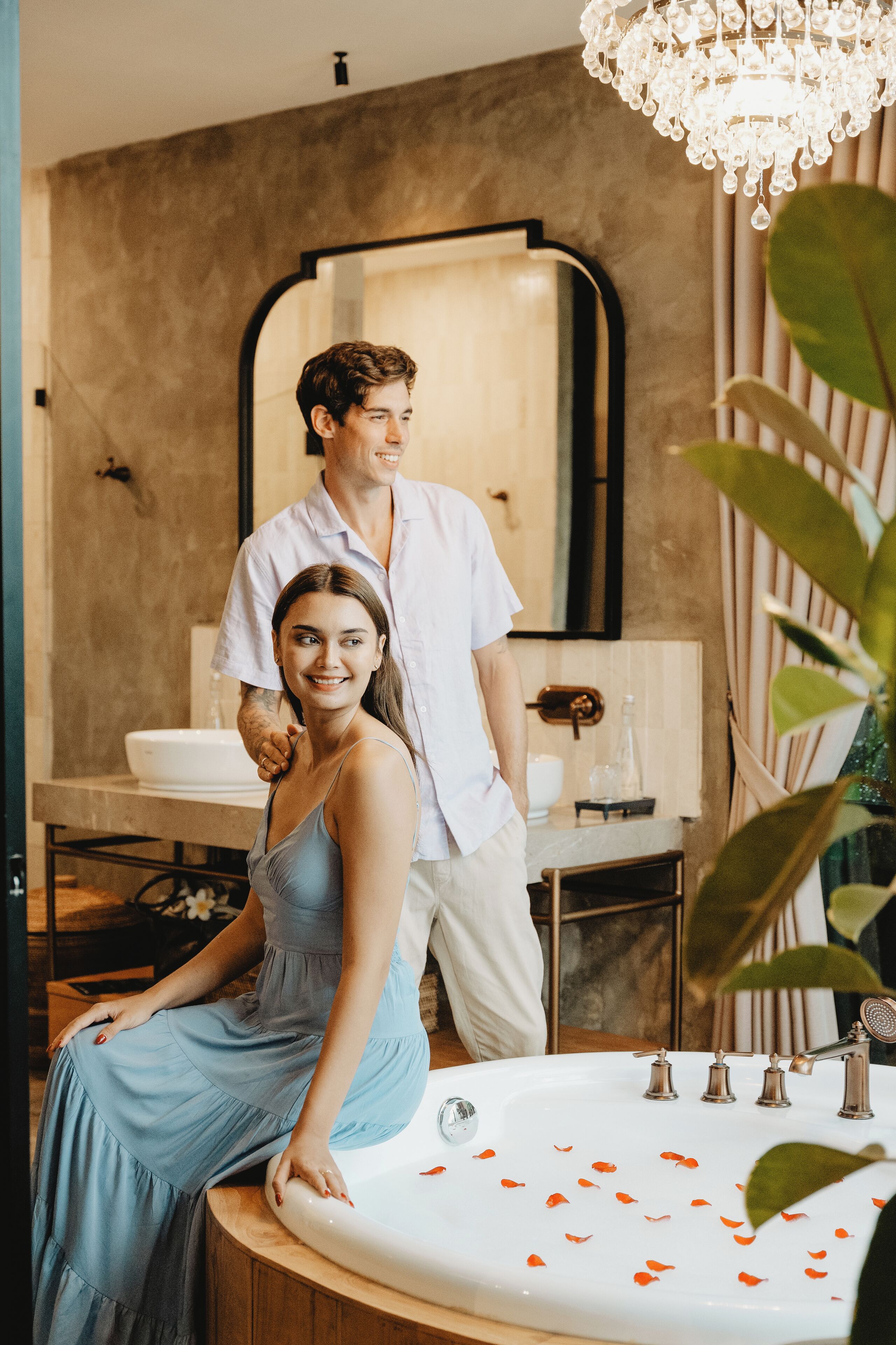 Un baño con un espejo grande, un lavabo decorado con pétalos de rosa y un candelabro.