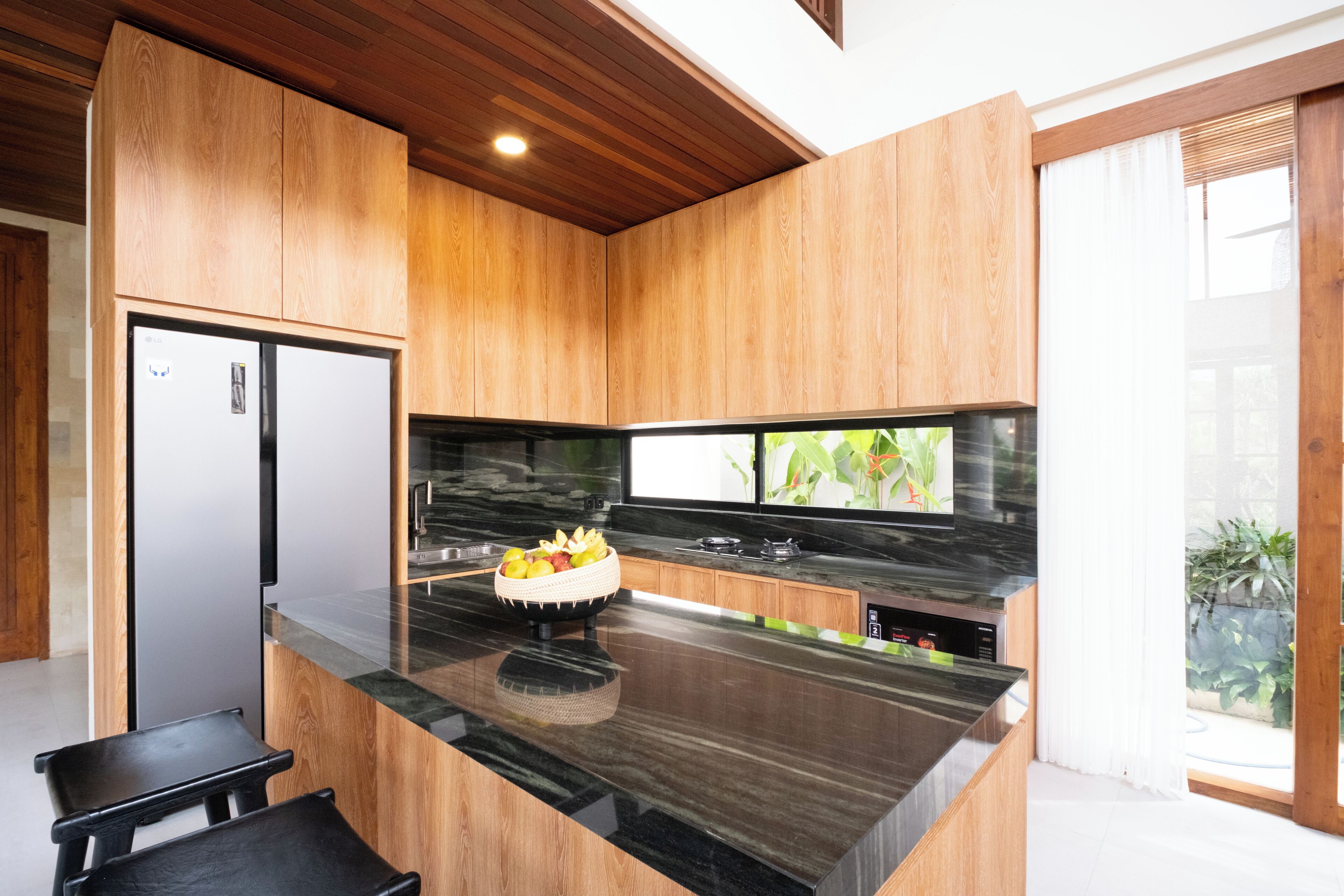 Una cocina moderna con armarios de madera, encimera de mármol negro y estufa empotrada.
