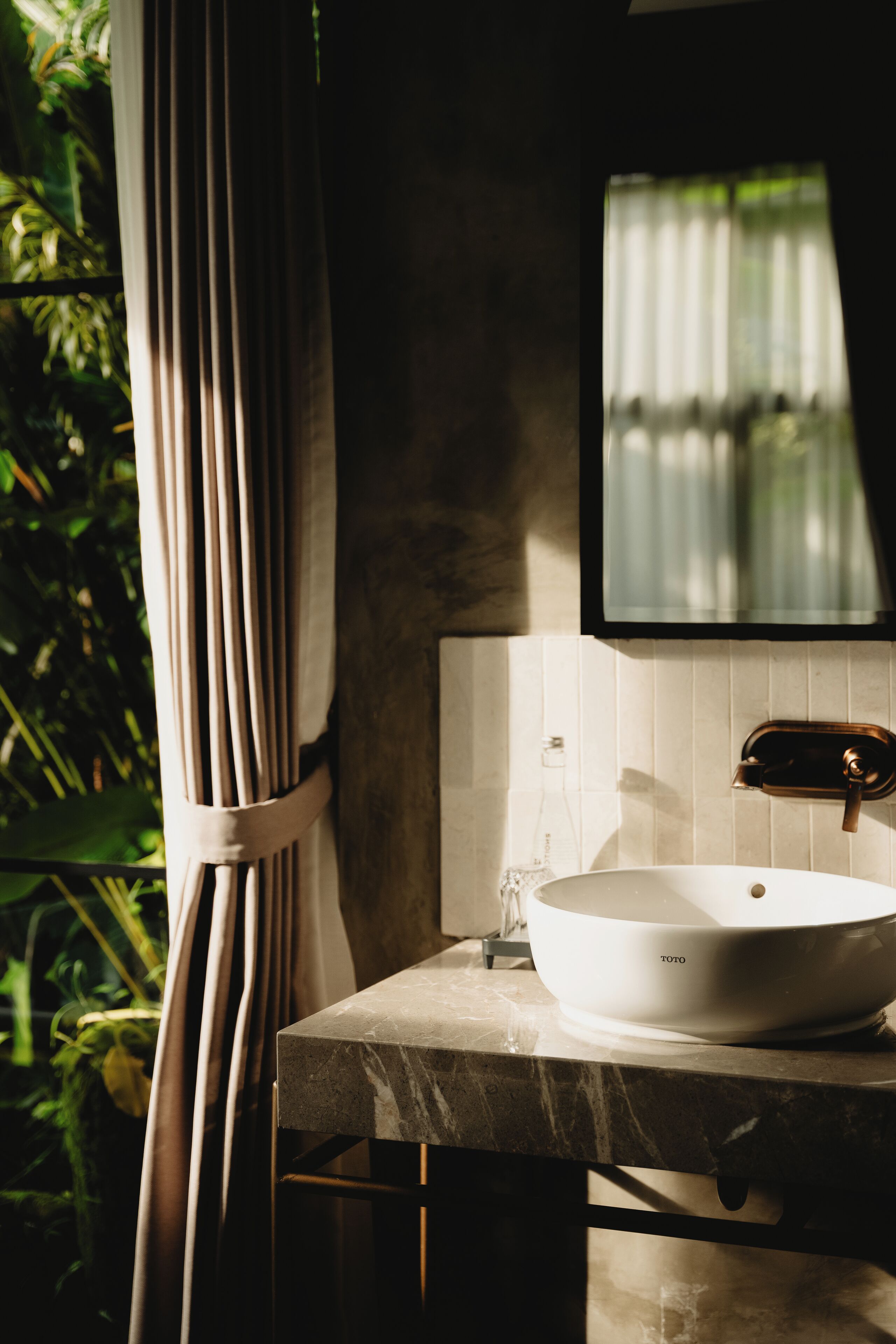 A bathroom with a white sink, a mirror, and a window with curtains.