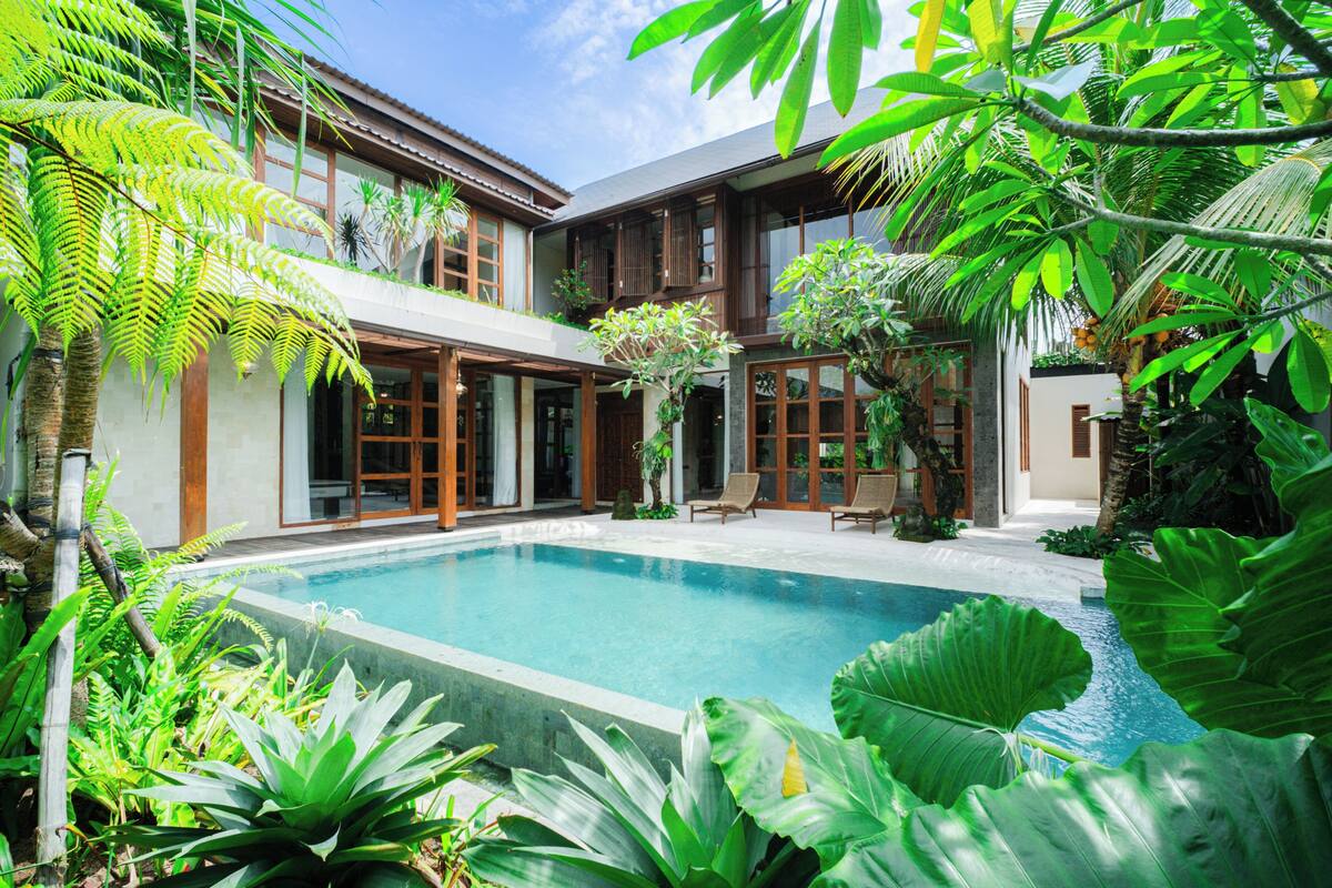 A modern house with a swimming pool surrounded by lush tropical plants.