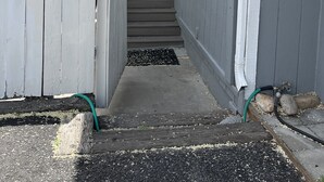 Un étroit sentier mène à une maison entourée d’une clôture blanche en bois, avec une porte et une fenêtre.