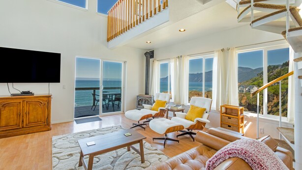 A spacious living room with a large TV, comfortable seating, and a view of the ocean.