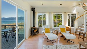 A spacious living room with a fireplace, large windows, and a view of the ocean.