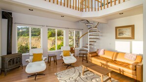 A spacious living room with a wooden staircase, large windows, a white sofa, and a vintage radio.