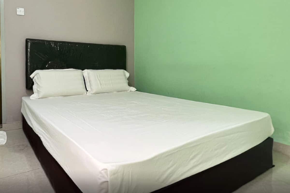 A bed with a white mattress and pillows, a black headboard, and a green wall.