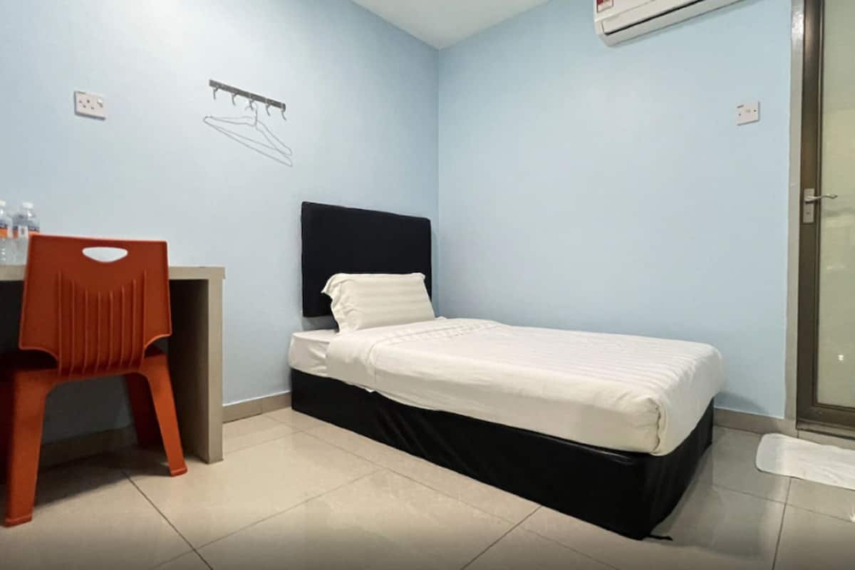 A small, single-bed room with a desk and chair, a black headboard, and a shower area.
