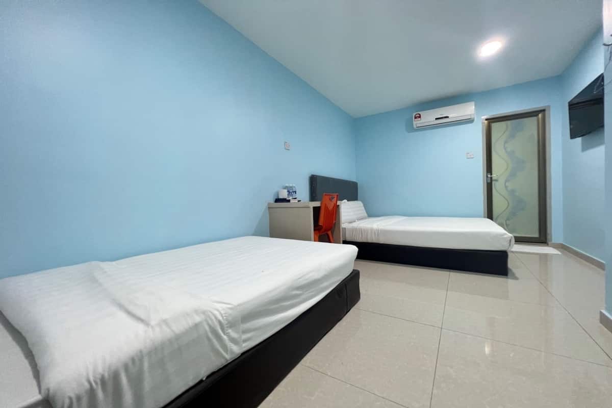 A room with two single beds, a small table with a chair, an air conditioning unit, and a door with a glass panel.