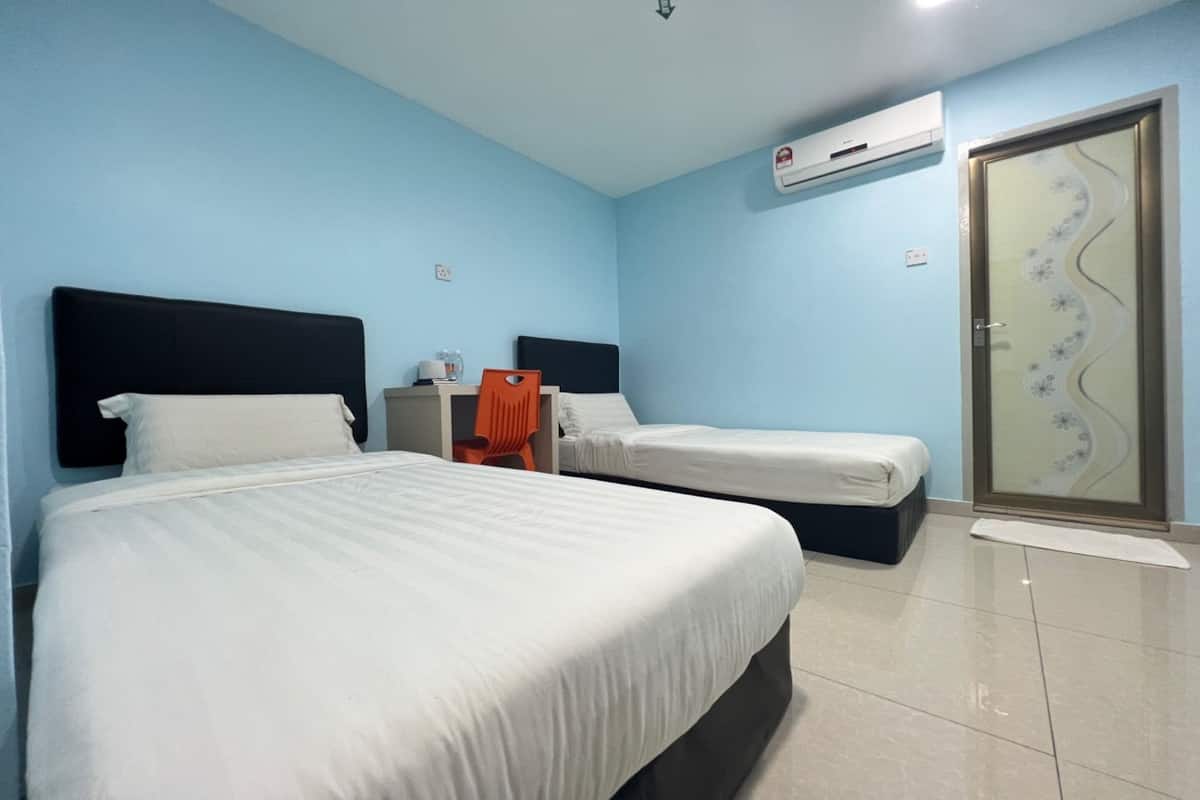 A hotel room with two beds, a small table, an orange chair, and a door with a decorative glass panel.