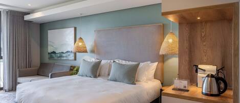 A modern hotel room with a large bed, two bedside tables, a sofa, and a painting on the wall.