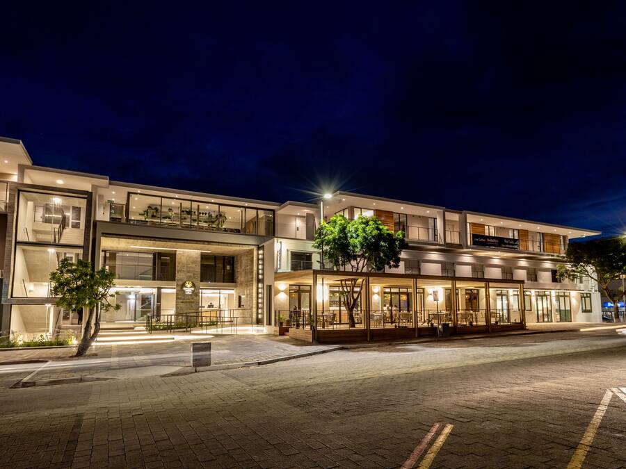 A modern hotel with multiple floors, large windows, and outdoor seating areas.