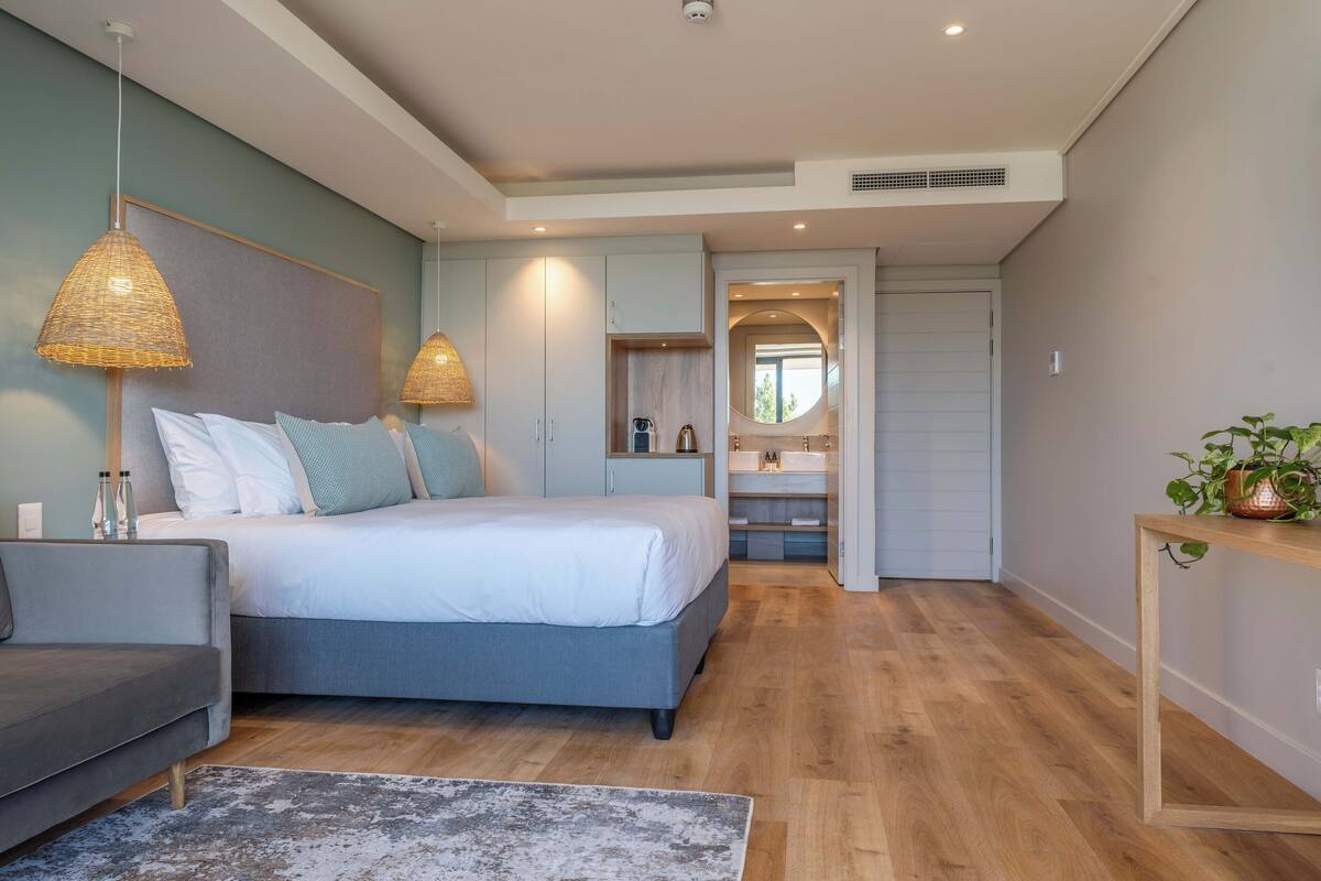 A modern bedroom with a bed, bedside tables, a sofa, and a bathroom with a sink and mirror.