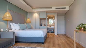A modern bedroom with a bed, bedside tables, a sofa, and a bathroom with a sink and mirror.