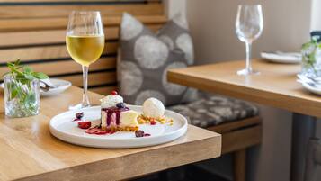 A dining table with a dessert plate containing a slice of cake with berries and a scoop of ice cream, accompanied by a glass of white wine.