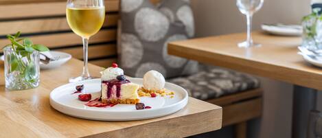 A dining table with a dessert plate containing a slice of cake with berries and a scoop of ice cream, accompanied by a glass of white wine.