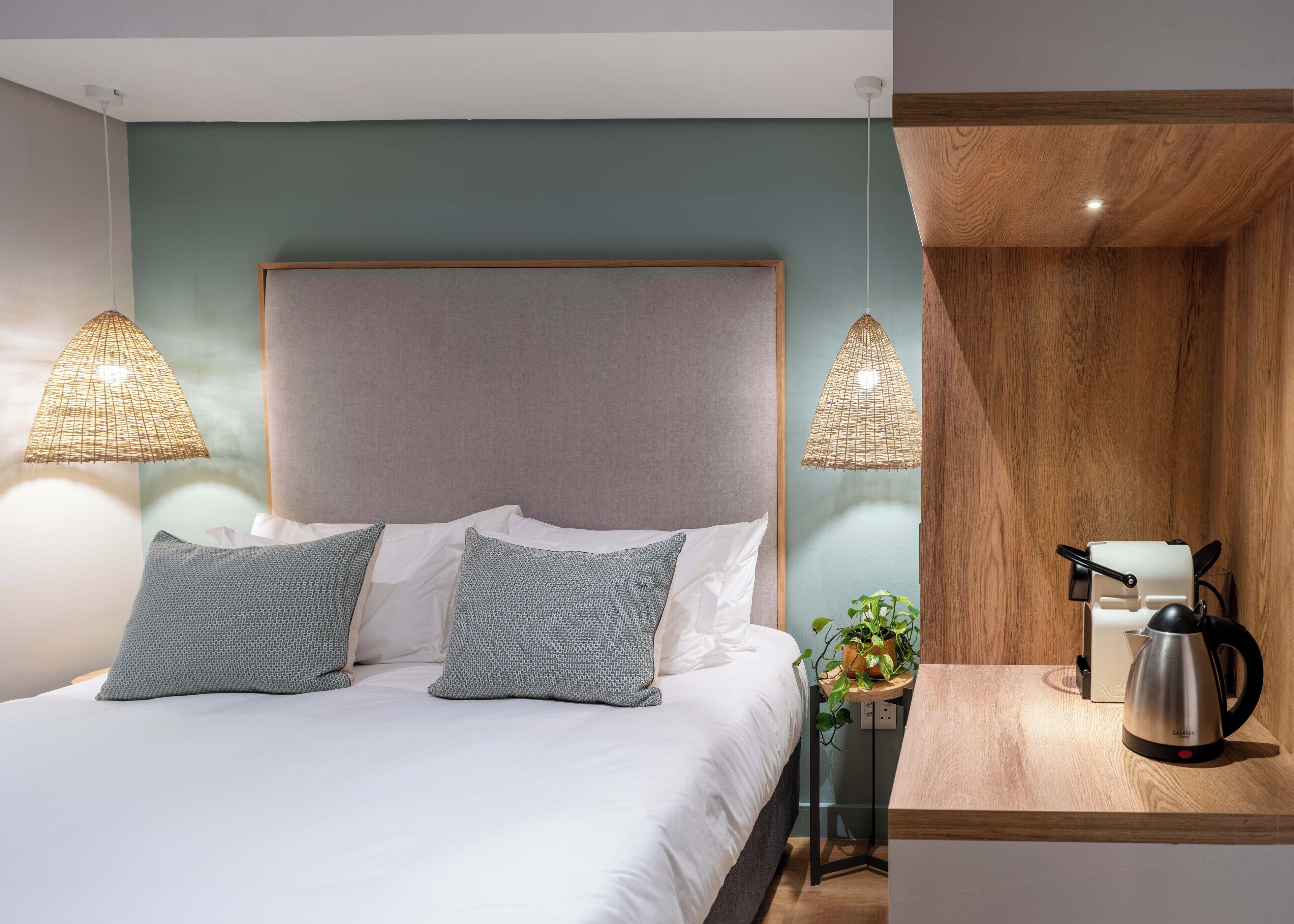 A modern bedroom with a large bed, two bedside lamps, a wooden nightstand, and a kettle.