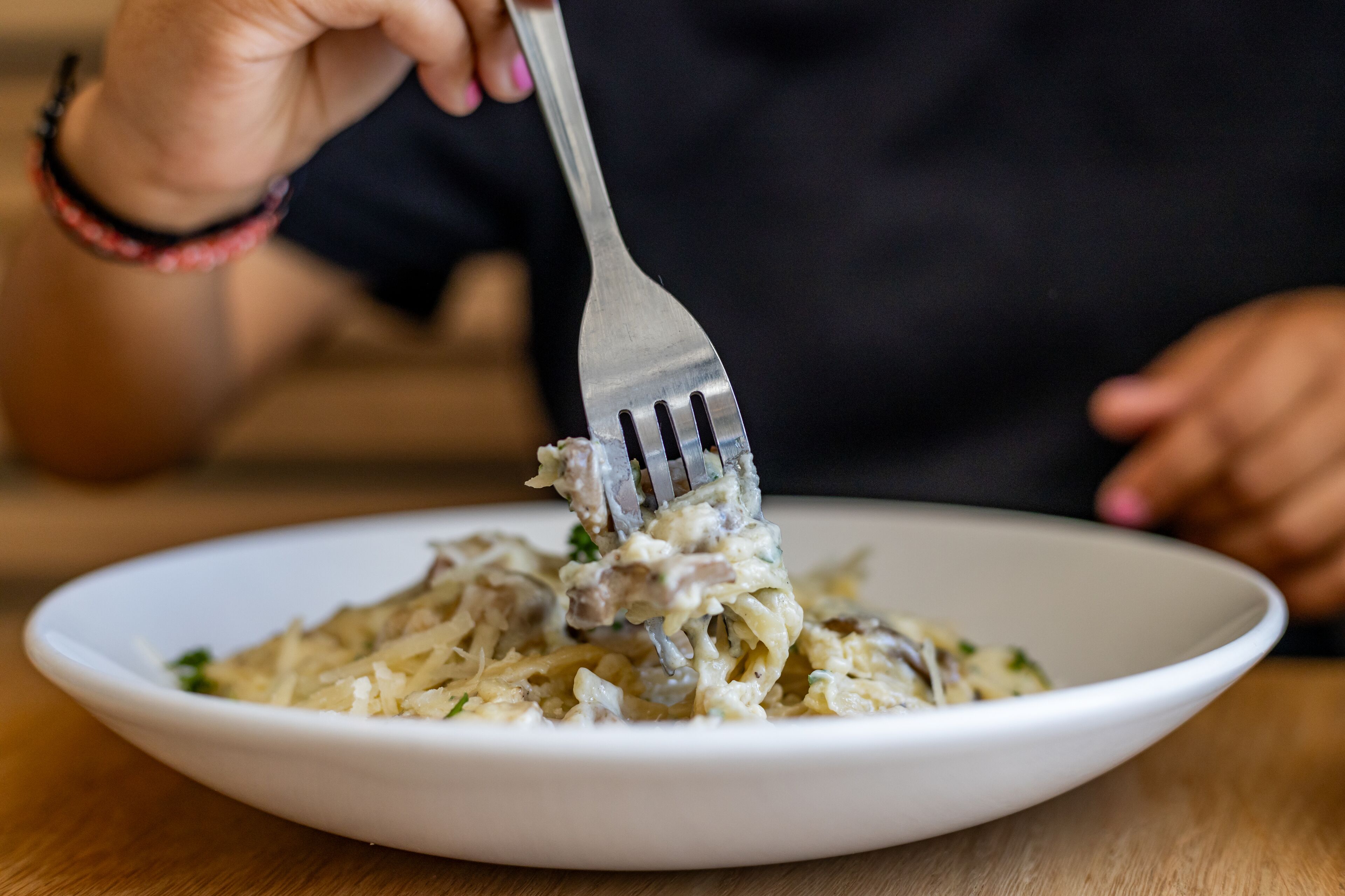 A person using a fork to eat pasta from a white bowl.