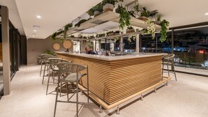 A modern bar area with a wooden counter, bar stools, and hanging plants.