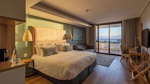 A modern hotel room with a large bed, a desk, a chair, and a balcony with a view.