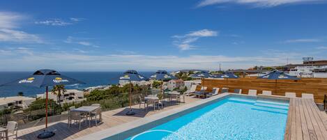 A swimming pool with lounge chairs and umbrellas, overlooking a beach and ocean.