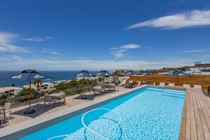 A swimming pool with lounge chairs and umbrellas, overlooking a beach and ocean.