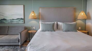 Una habitación de hotel moderna con una cama grande, dos lámparas de noche, un sofá y un cuadro en la pared.