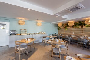 A modern cafe with wooden tables and chairs, a counter with food items, and hanging plants.