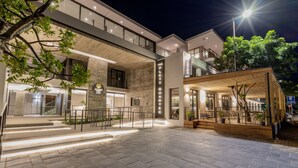 A modern hotel entrance with a stone facade, a covered outdoor seating area, and a staircase leading to the upper floors.