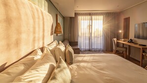 A hotel room with a large bed, a desk with a chair, a television, and a window with curtains.