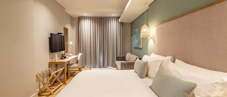 A modern hotel room with a large bed, a desk, a chair, a television, and a window with curtains.
