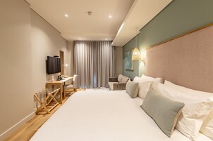 Una habitación de hotel moderna con una cama grande, un escritorio, una silla, un televisor y una ventana con cortinas.