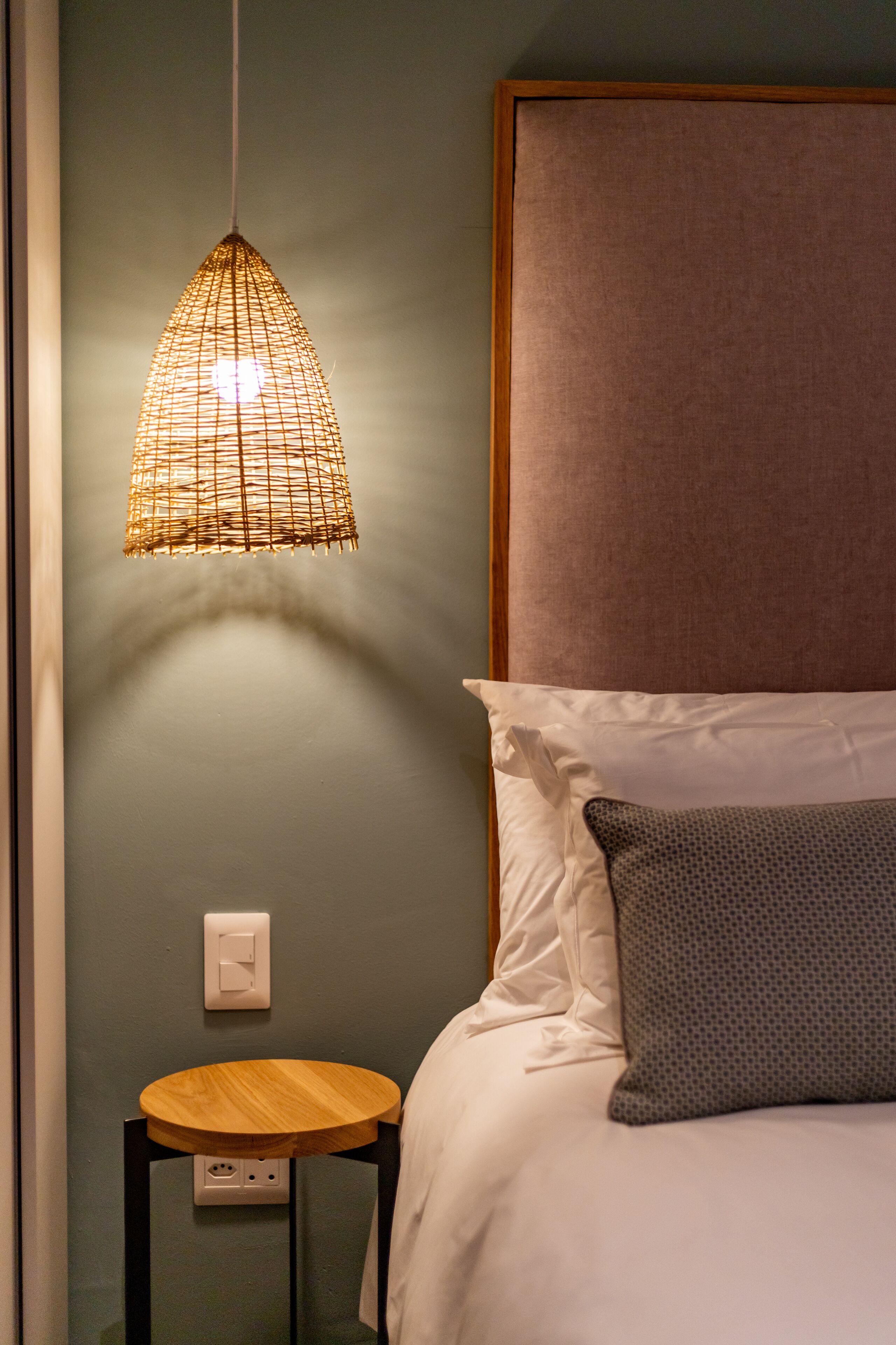 Un dormitorio con cama, mesita de noche, lámpara colgante y enchufe de pared.
