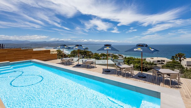 A pool area with a view of the ocean, surrounded by lounge chairs and umbrellas.