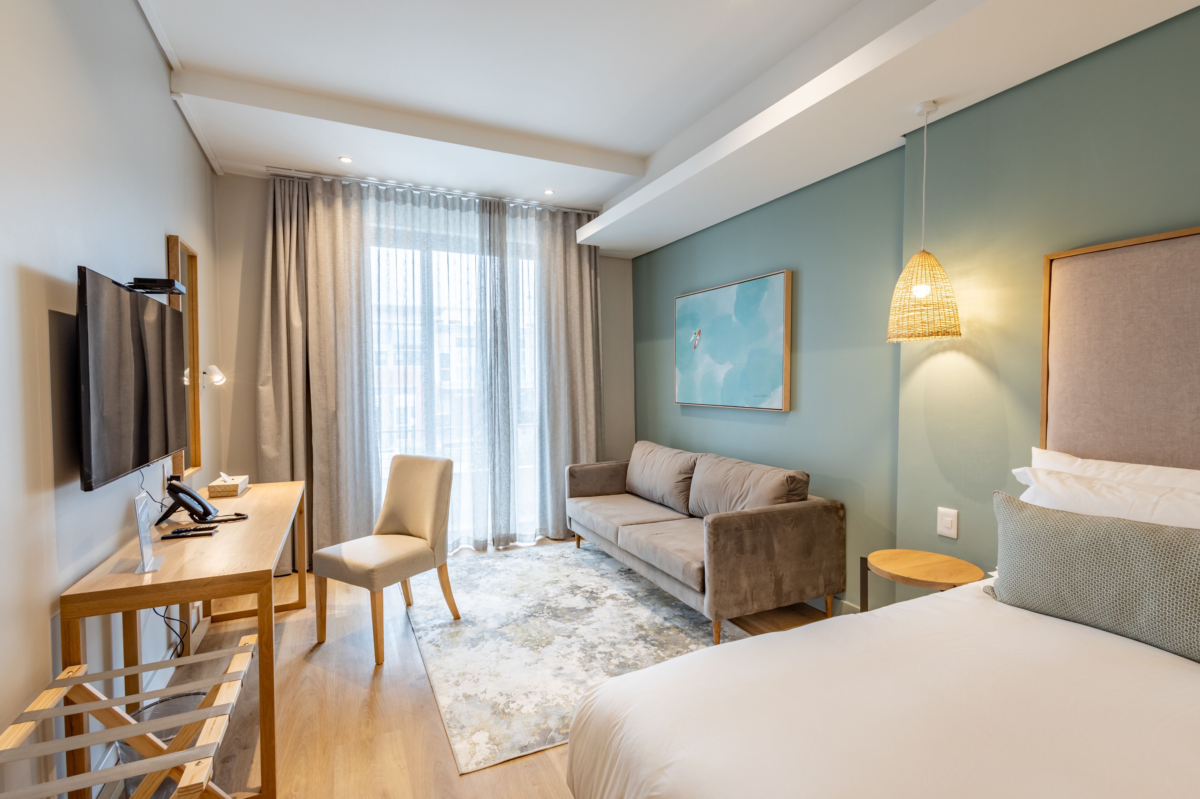 A modern hotel room with a bed, a desk with a chair, a sofa, and a television.