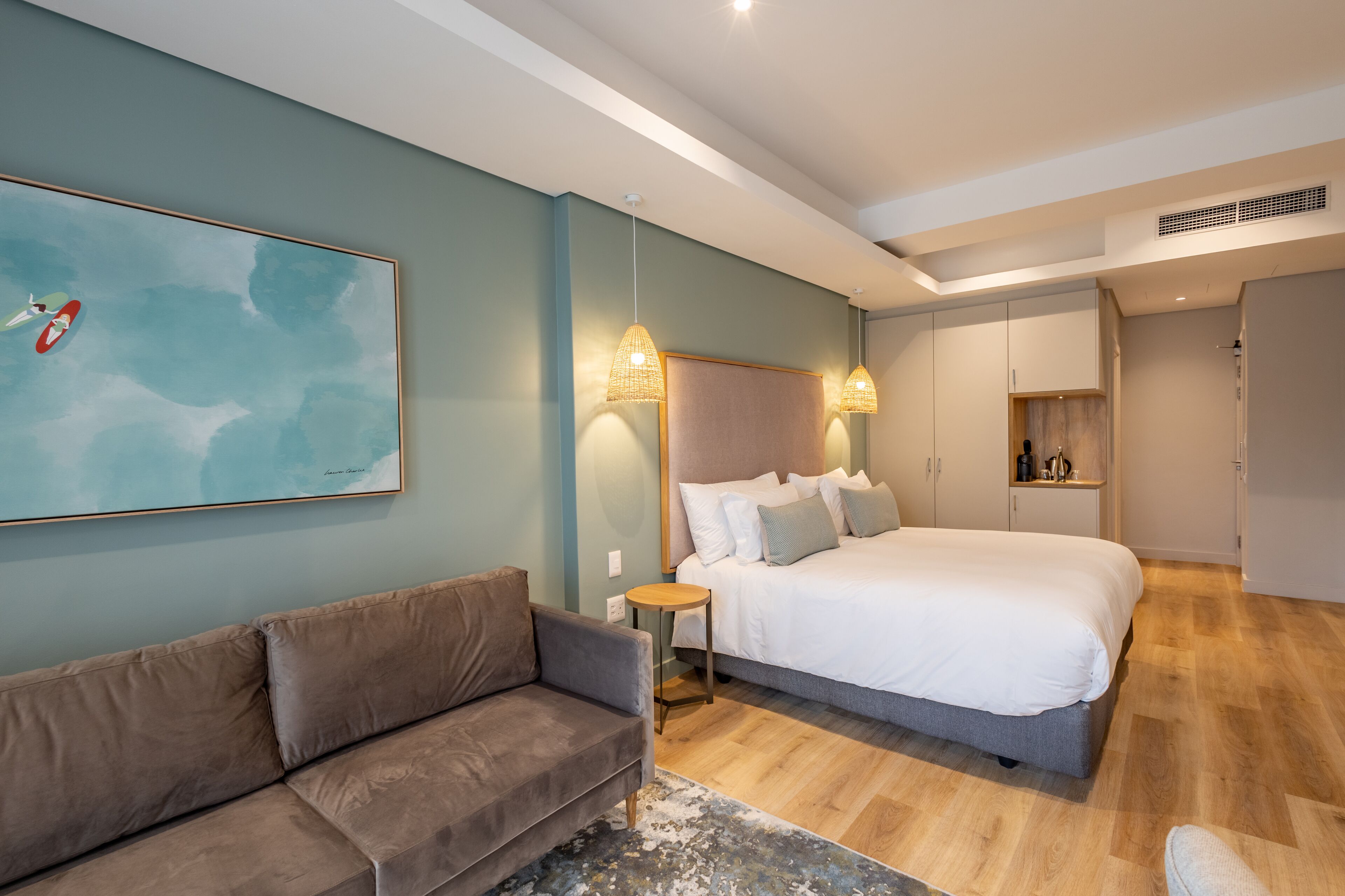 A modern bedroom with a large bed, a sofa, and a painting on the wall.