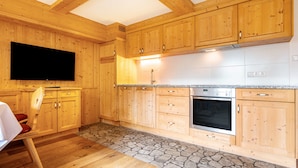 A kitchen with wooden cabinets, a stone backsplash, a built-in oven, and a flat-screen TV.
