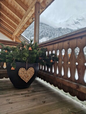 Un balcon en bois agrémenté d’un grand bac contenant un arbre et une composition décorative en forme de cœur, réalisée avec des bûches.