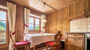 Una cabaña de madera con mesa, sillas, zona de cocina y ventana con cortinas.