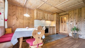 Un interior de madera con una mesa de comedor, un banco, una silla de madera, una planta en maceta y una zona de cocina.