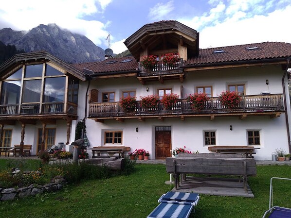Un chalet traditionnel doté d’un balcon orné de fleurs rouges, d’un banc en bois et d’un mur de pierres au premier plan.
