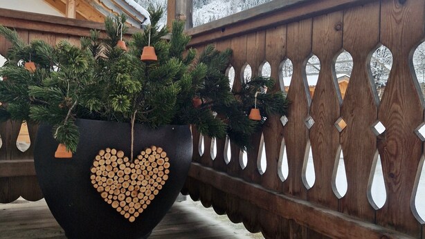 Un balcó de fusta amb una gran jardiniera que conté un arbre i una composició de troncs formant un cor.