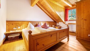 Un dormitorio de madera con techo inclinado, una cama con almohadas, una mesita de noche, una lámpara y una ventana con vistas a zonas verdes.