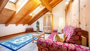 Habitación estilo loft con vigas de madera, un sofá rojo con estampado, un tapete azul y un mueble de madera.