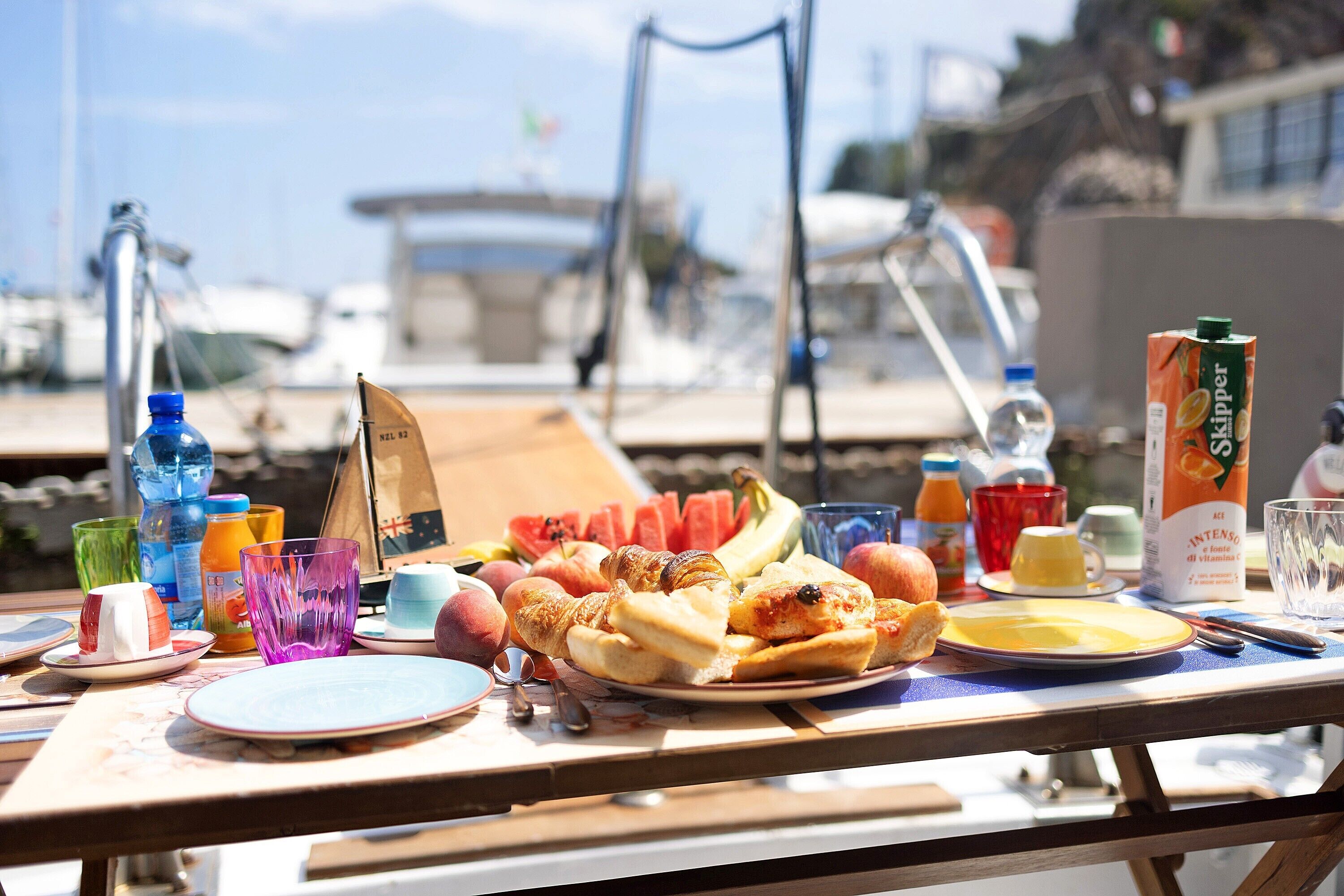 A table with food, drinks, and a flag, set against a marina backdrop.