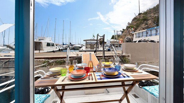 A dining table set with plates, glasses, and cutlery on a boat with a view of a marina. - Aloha Jak's Boat with Sea View, Wi-Fi, and Air Conditioning (Alassio)