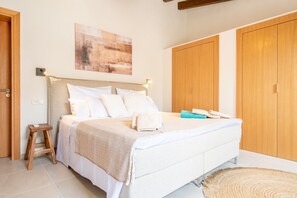 Een slaapkamer met een bed, een houten krukje, een wandlamp en een deur.