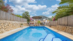 Une piscine aux murs en pierre et à la clôture en bois, entourée de plantes en pot et sous un ciel dégagé.