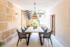 A dining area with a wooden table and wicker chairs, a stone wall, and a staircase leading outside. - Holiday Home 'Alica 8' with Private Pool, Wi-Fi and Air Conditioning (POLLENÇA)