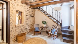 Un mur de pierres, un escalier en bois, deux fauteuils à bascule, une petite table avec une plante et un panier en osier.