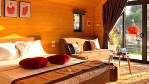Une chambre aménagée dans une cabane en bois, avec un grand lit, une petite table et une vue sur l’extérieur.